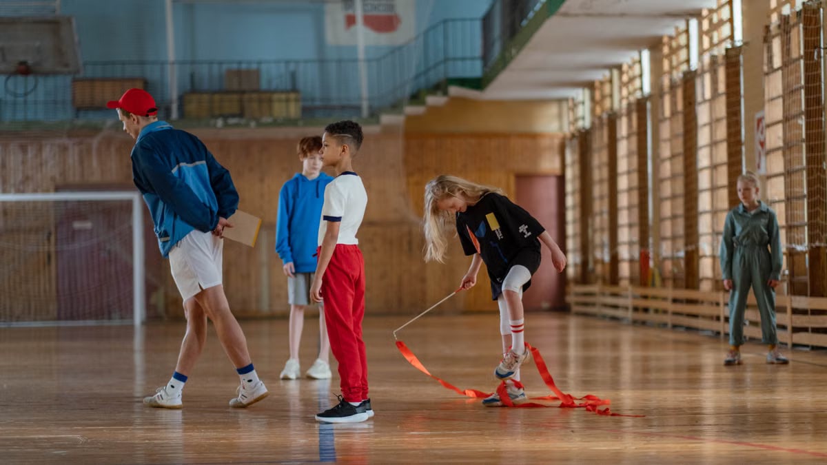 Children practicing gymnastics in a sports hall with their teacher.